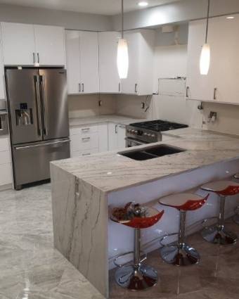 Bright white kitchen with white wood cabinets, white and grey quartz stone contertops, and red bar stools.